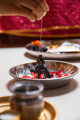 Indian woman performing snan ritual by pouring 'Honey' on (Laddu Gopal) Hindu god Krishna, during the Indian festival of Krishna Janmashtami.