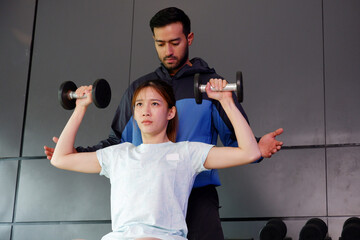 Young woman and trainer exercising with dumbbells in a fitness gym. © krongthip