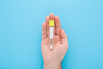 Young adult man opened palm holding empty transparent plastic tube for urine or other analysis test on light blue table background. Pastel color. Healthcare concept. Closeup. Top down view.