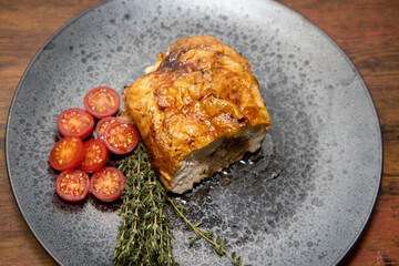 A delicious meat roast stuffed with stuffing with tomatoes and garnish on a wooden background