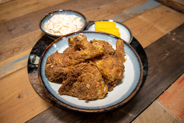 A plate of crispy fried chicken legs with coleslaw and sweetcorn on a wooden kitchen work top