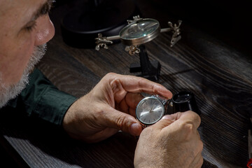 Watchmaker repairing watches looking through magnifying glass monocular. Professional senior watch fixer in repair services workshop.