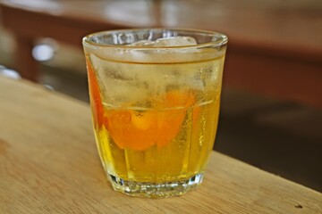 A glass of iced tea with a slice of orange, served on a rustic wooden table. The refreshing drink glistens in the sunlight, offering a thirst-quenching, citrusy, and cool sensation.