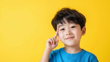 Young boy with short dark hair smiles and poses thoughtfully against a bright yellow background in a casual blue shirt.