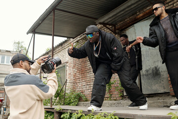 Group of African American men performing outdoors for music video captured by videographer