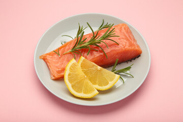 Red fish. Raw salmon fillet with rosemary and lemon on plate on pink background.