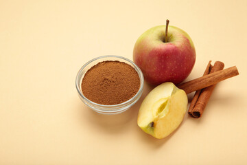 Apples with cinnamon in bowl on beige background.