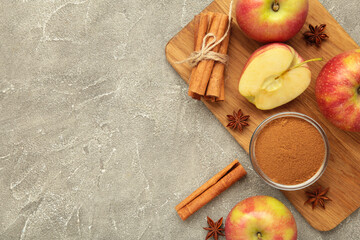 Red apple, cinnamon sticks and cinnamon in bowl on grey concrete background.