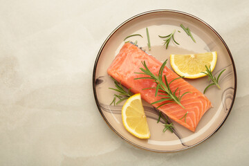 Red fish. Raw salmon fillet with rosemary and lemon on beige plate on grey background.