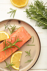 Red fish. Raw salmon fillet with rosemary and lemon on white background. Vertical photo