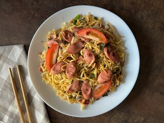 Stir-fried noodles with sausage and vegetables on dark background. Top view. Asian food style