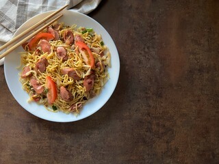 Stir-fried noodles with sausage and vegetables on dark background. Top view. Asian food style