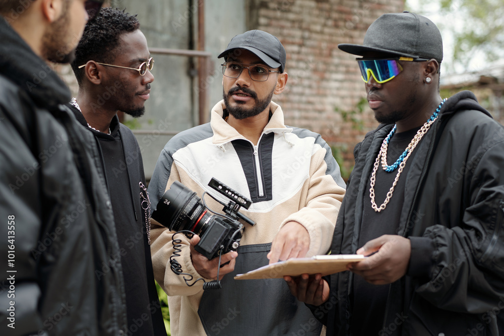 Poster group of men engaging in a conversation on set about film project while holding camera and clipboard