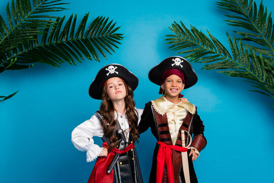 Portrait of two little kids halloween pirate costume posing palm leaves isolated on blue color background