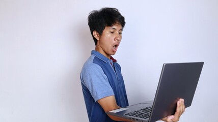 shocked asian young man holding and looking at laptop