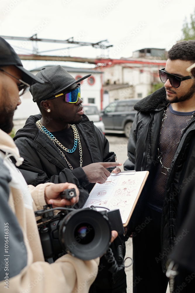 Poster Group of people engaging in project discussion while holding documents and camera outside. Urban backdrop and casual attire highlight collaborative and creative environment