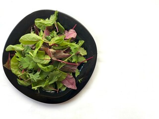 Fresh salad of mixed greens in a black plate on a white background
