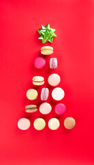 Christmas background with macaroons on red, french cakes in the shape of a Christmas tree with a green bow. Vertical orientation, top view.