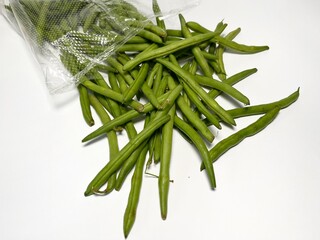 Fresh green beans scattered on a white background. Green beans in a plastic bag on a white background, close-up