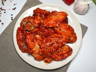 Raw marinated spicy chicken wings on a plate with spices and vegetables on a white background.  Fast cooking. Raw marinated chicken meat.