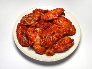 Marinated spicy chicken wings on a plate on a white background, isolated. Top view. Copy space. Semifinished. Fast cooking. Raw marinated chicken meat.