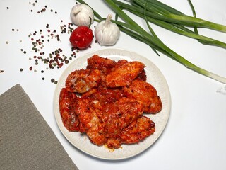 Raw marinated spicy chicken wings on a plate with spices and vegetables on a white background.  Fast cooking. Raw marinated chicken meat.