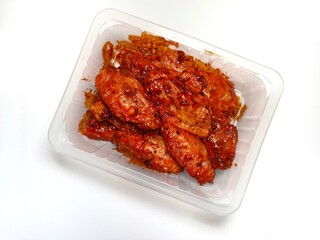 Marinated spicy chicken wings in a plastic container on a white background.