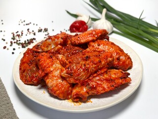 Raw marinated spicy chicken wings on a plate with spices and vegetables on a white background.  Fast cooking. Raw marinated chicken meat.