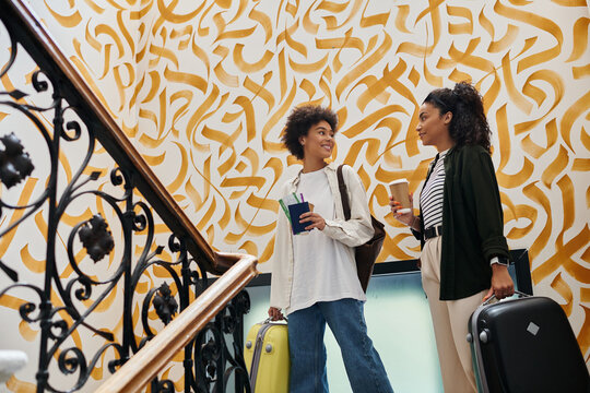 A joyful couple stands in a vibrant hostel, chatting and ready to explore their travel adventure.