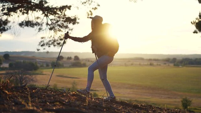 Silhouette of a tourist with backpack and poles. Mountain person trekking concept. A girl is backpacking through a forest. Silhouette of young girl with backpack and tourists lifestyle in the forest.