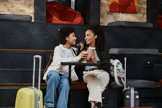 A joyful lesbian couple at a hostel cafe, sharing smiles and warm drinks during their travels.