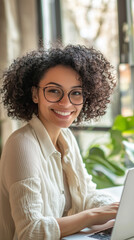 Young Woman with Curly Hair Smiling and Working on Laptop in Modern Workspace