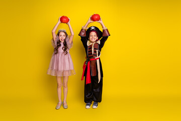 Full size photo of two kids halloween princess pirate costume hold pumpkin empty space isolated on yellow color background