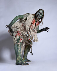 portrait of scary female model wearing spooky halloween costume, ripped clothes and fake blood like an undead demon apocalyptic zombie character. Isolated figure, crouching pose dark studio background © faestock