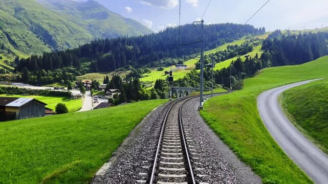 Front View on Glacier Express Train with Railroad Tracks and Beautiful Mountainscape and Village in a Sunny Summer Day in Sedrun, Surselva, Oberalp, Grisons, Switzerland.