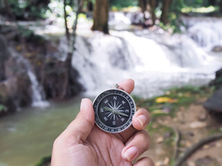 Close up of compass in woman hand with waterfall as background. The concept of world tourism day, Searching the right directions and Travel