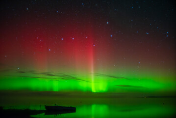 beautiful green red northern lights on the lake in autumn night with a lonely boat