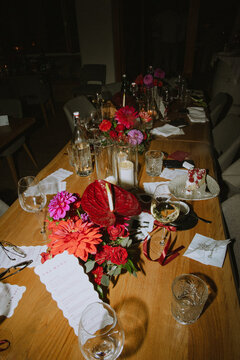 A long table decorated with vibrant red and pink flowers, candles, and wine glasses, set for a wedding. photographed with flash
