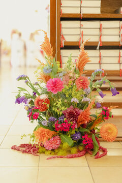 Vibrant flower arrangement placed beside stacked hymn books in a bright indoor space, likely a church or ceremonial setting.