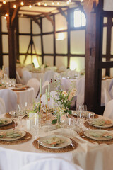 Beautiful rustic wedding reception with round tables, floral centerpieces, and warm lighting in a wooden-beamed venue.