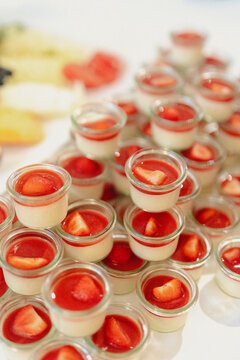 A visually appealing dessert table with stacked mini panna cotta cups topped with fresh strawberry sauce.