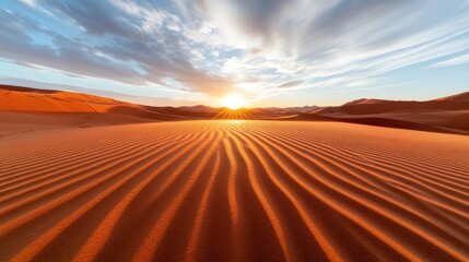 Naklejka premium A breathtaking sunrise casts golden hues over rippled desert dunes, highlighting the intricate patterns in the sand under a sky filled with dynamic clouds.