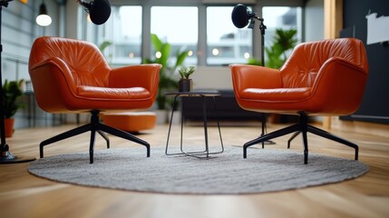 Two orange armchairs positioned in a well-lit room with microphones, set for interviews or discussions, surrounded by plants for an inspiring and warm atmosphere.