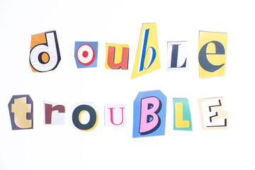 Phrase Double Trouble spelled in cut out newspaper style typography isolated on white background.