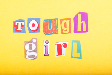 Phrase Tough Girl spelled in cut out newspaper style typography, isolated on yellow background.