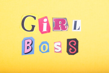 Phrase Girl Boss spelled in cut out newspaper style typography, isolated on yellow background.