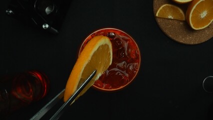 Macrography, experience the art of decorate a Negroni cocktail from a top-down perspective, adorned with a fresh vibrant orange slice, all against a dramatic black background. Alcoholic. Comestible.