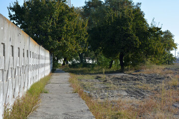 Beautiful, bright Ukrainian nature. Blue beautiful sky, saturated green trees, steppe with dry grass with a gray cement fence and paths.
