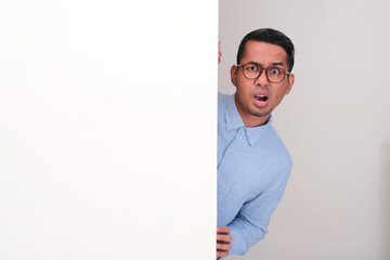 A man peeking behind wall seeing something with confused expression