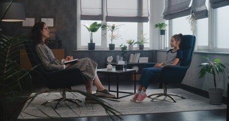 Psychological office: Asian schoolgirl sits in chair, talk to female therapist. Professional...